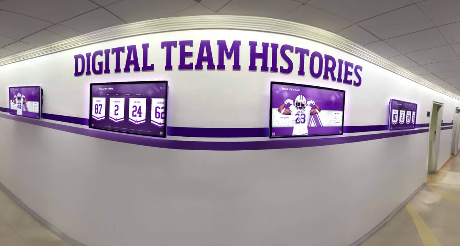 Multiple digital screens displaying team histories and timelines in school hallway