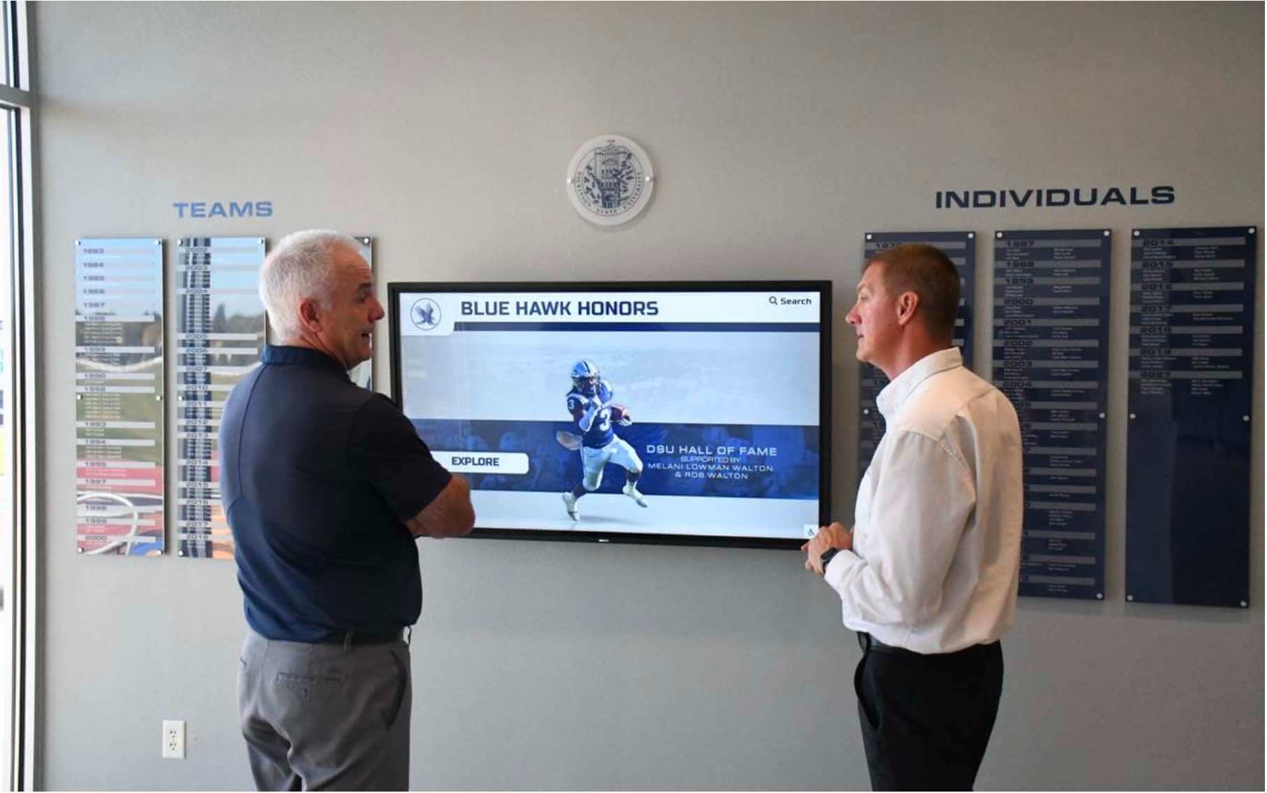 Two men engaging with athletic hall of fame touchscreen display